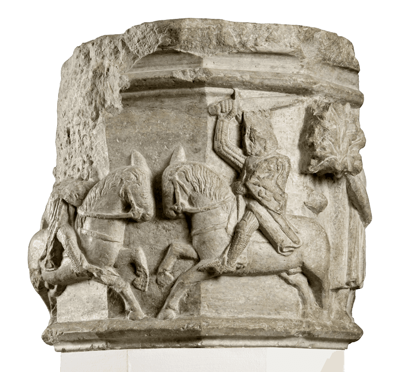 Carved limestone column capital showing two mounted knights in armor, one brandishing a raised sword.