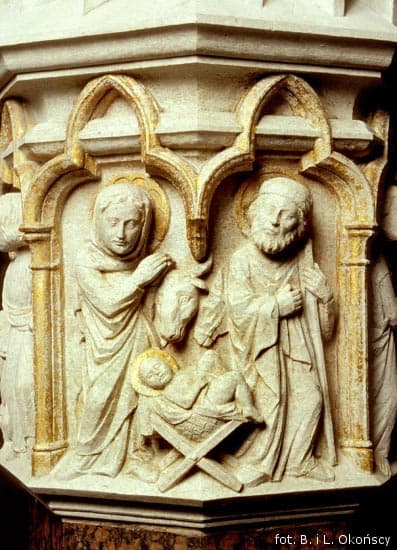 Stone carved Nativity relief on a column capital showing Mary, Joseph, and the newborn in a manger.